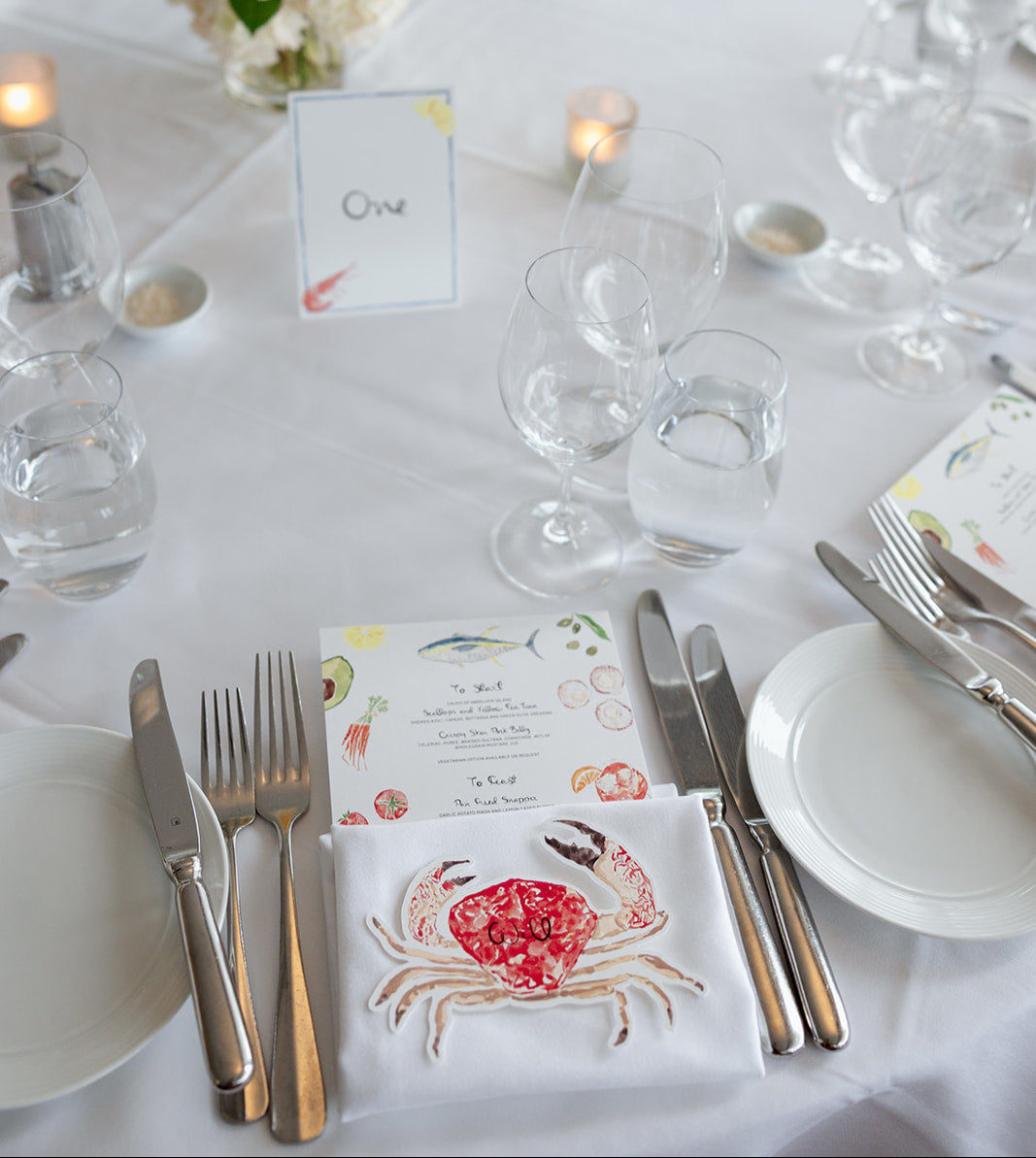 Elegant table setting with floral centerpiece, place cards, and cutlery on a white tablecloth.
